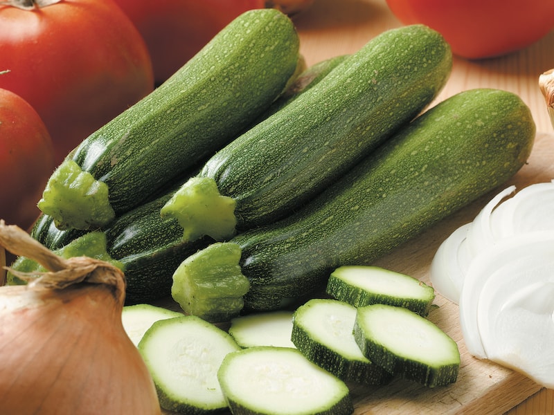 Courgette 'F1 Defender' in a pile on a wooden table next to other vegetables