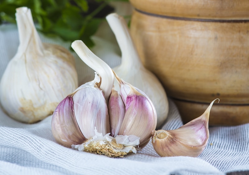 Pink garlic bulbs on a tablecloth next to wooden bowl