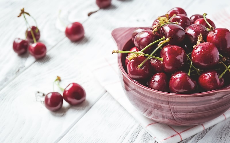 Cherries in a bowl on white wooden table