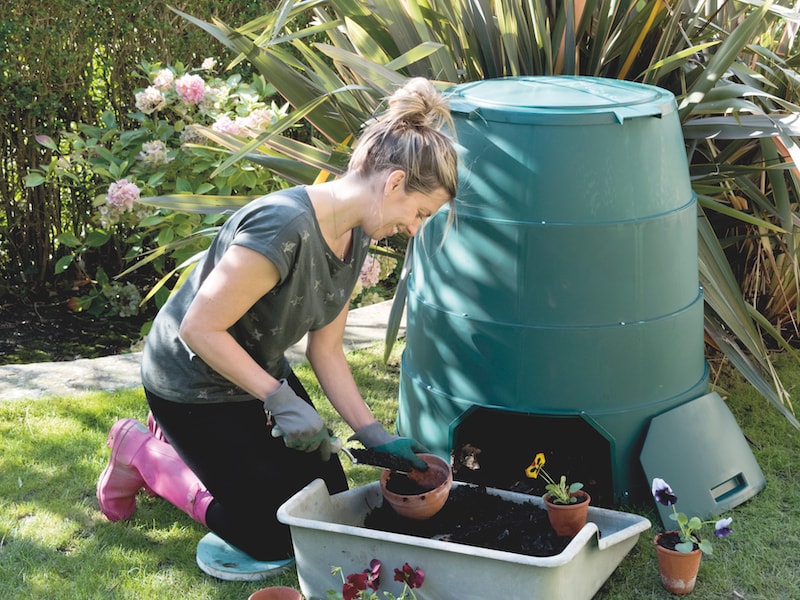 Woman kneeling next to compost bin potting on plants