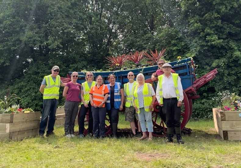 Community volunteers in hi-vis vests stand by a planted heritage cart.