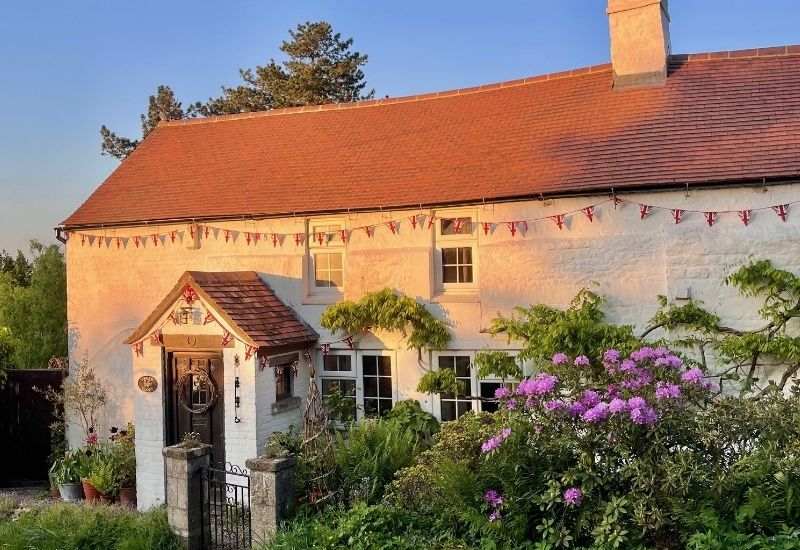 Traditional white Cotswolds cottage with a red tiled roof glowing in the golden hour sunset.