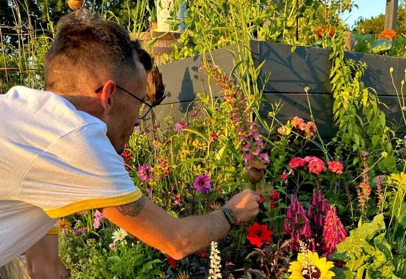 Person wearing glasses while gardening among colourful flowers.