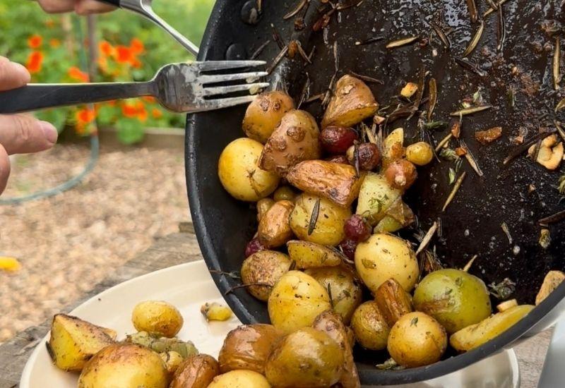 Roasted baby potatoes with garlic and rosemary being served from a cast iron pan.